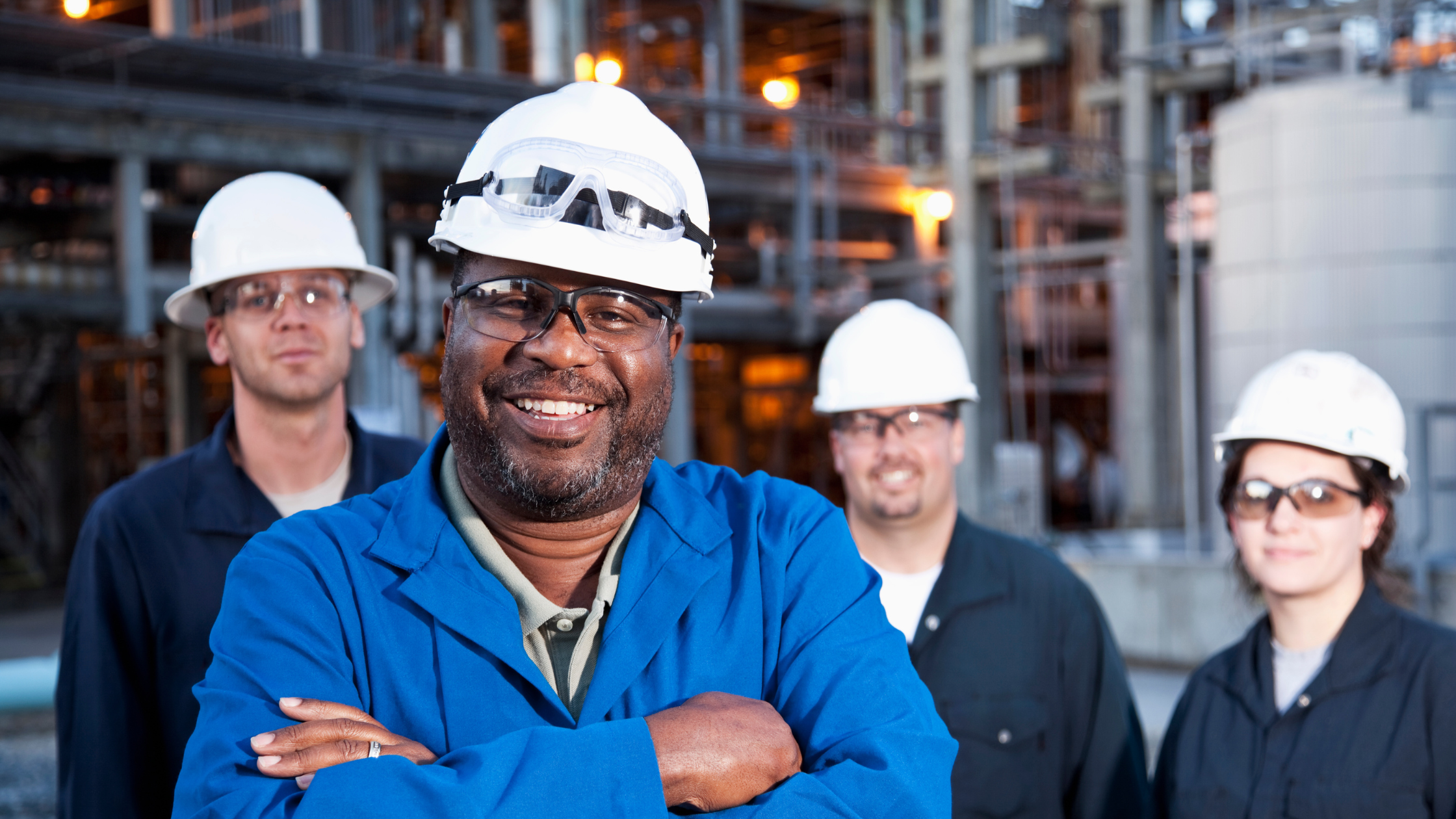One person in foreground and three people in background all posing for picture in hard hats.
